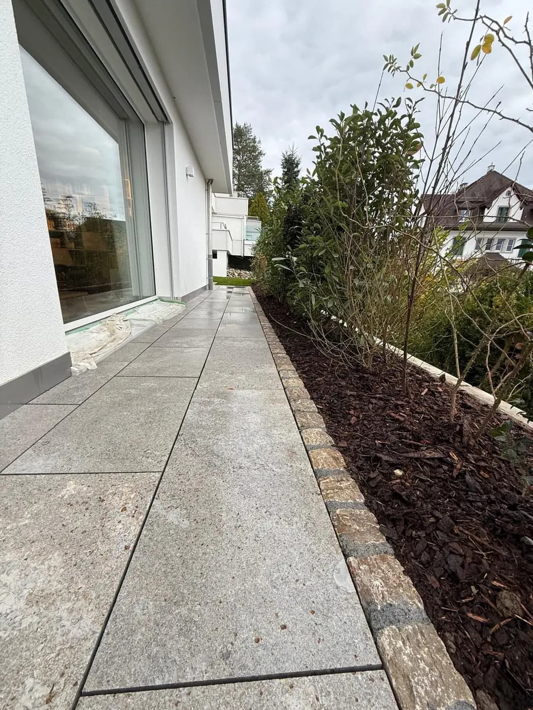 Bepflanztes Beet mit Rindenmulch entlang eines Granit-Plattenwegs in Freienbach – Soni Gartenbau