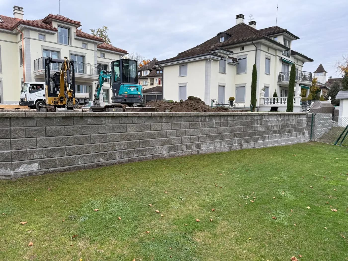 Fertiggestellte Blockstein-Stützmauer mit Firmenfahrzeug auf der Baustelle in Rapperswil – Soni Gartenbau