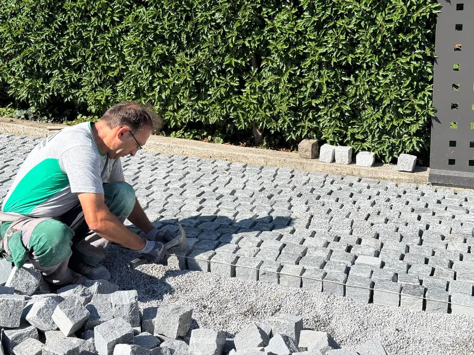 Handverlegtes Granit-Kleinpflaster im Splittbett, ein Mitarbeiter richtet die Steine an der gespannten Richtschnur aus – Soni Gartenbau
