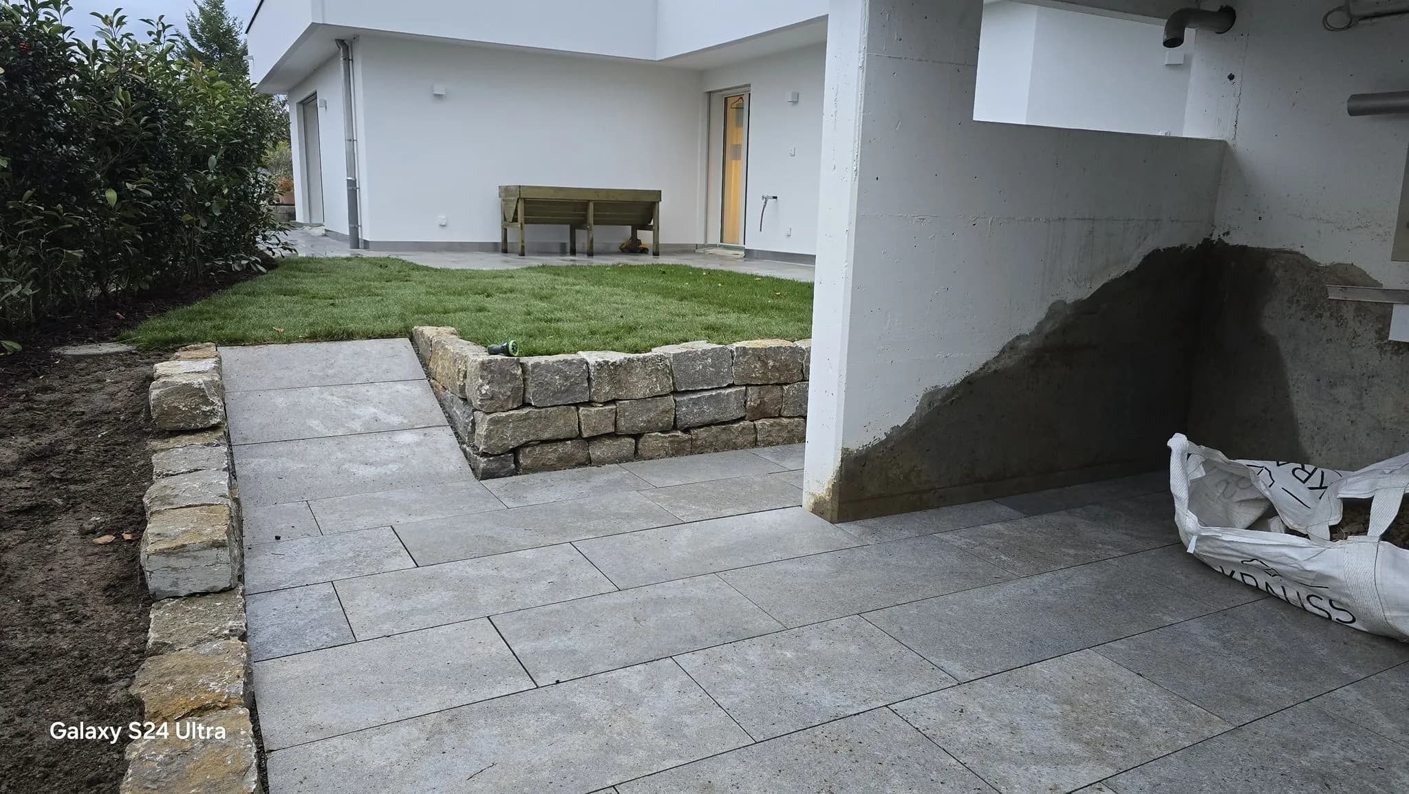 Gepflasterter Sitzplatz aus Natursteinplatten mit Trockenmauer und Rasen in Freienbach – Soni Gartenbau